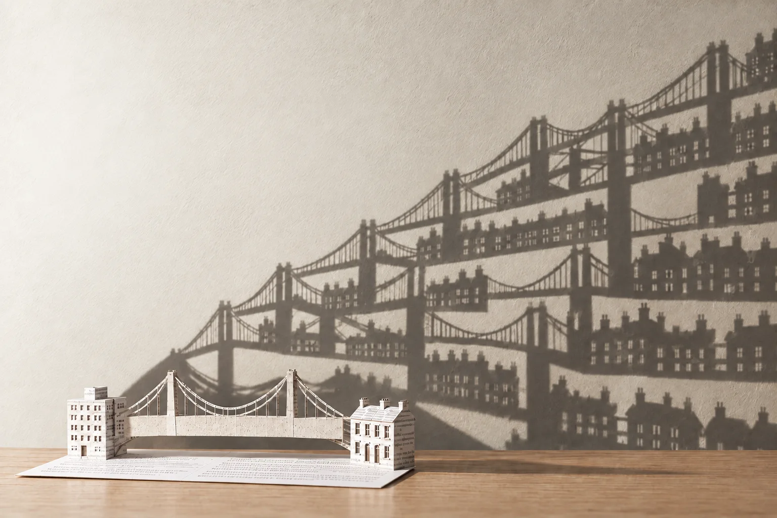 A small paper hospital and home linked by a paper bridge cast an immense, branching bridge shadow across the wall.